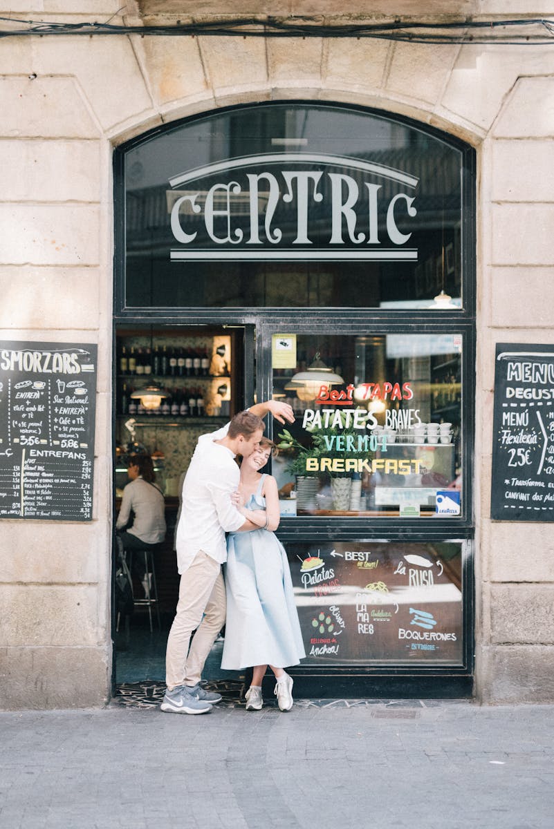 A loving couple embraces in front of a charming outdoor cafe, creating a romantic atmosphere.