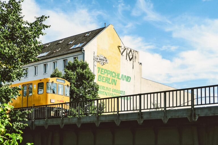 Yellow train passing by a building in Berlin, Germany, on a sunny day.