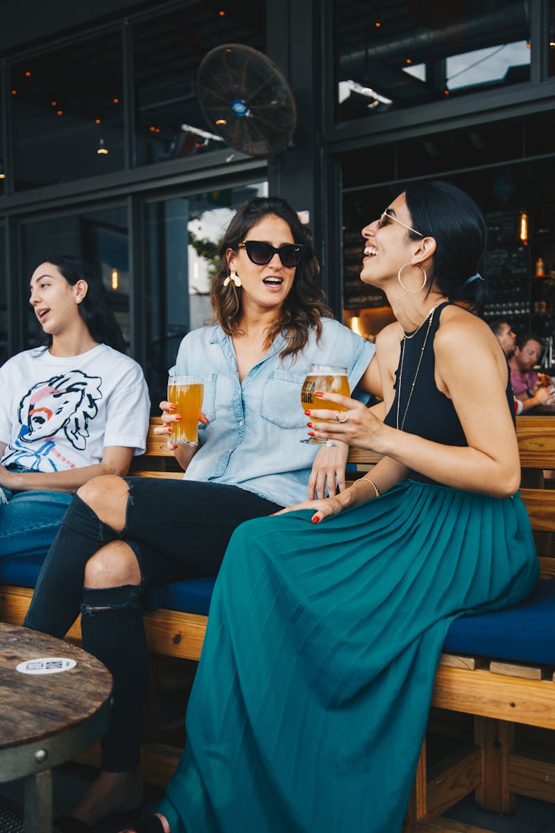 Three friends enjoying drinks and conversation at an outdoor bar.
