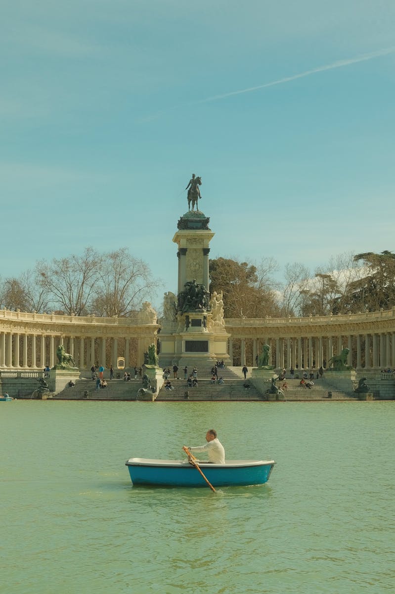 A serene scene of a person rowing in front of the Monument to Alfonso XII in Madrid's El Retiro Park.