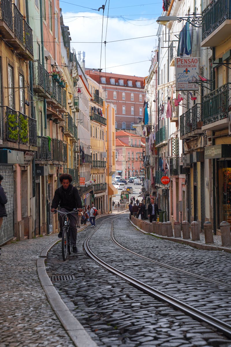 Cyclist rides through Lisbon's vibrant cobblestone streets lined with colorful buildings.