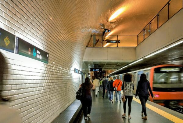 Commuters walking along a busy Lisbon subway platform with a moving train.