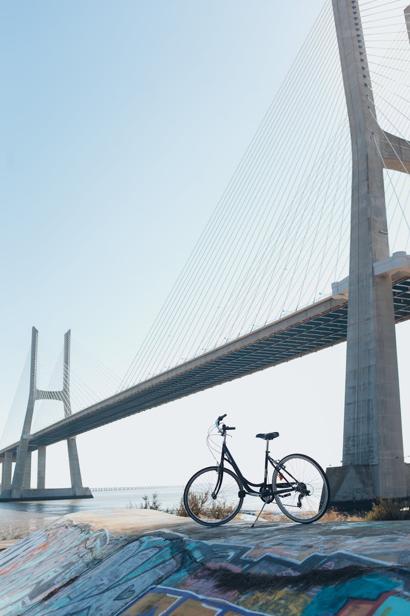 A bicycle with vibrant graffiti beneath a striking suspension bridge under a clear blue sky.