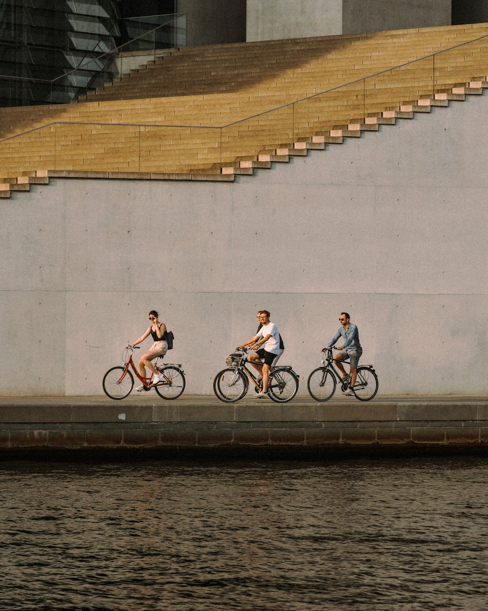 Three cyclists enjoy a summer ride along a canal in urban Berlin, framed by modern architecture.