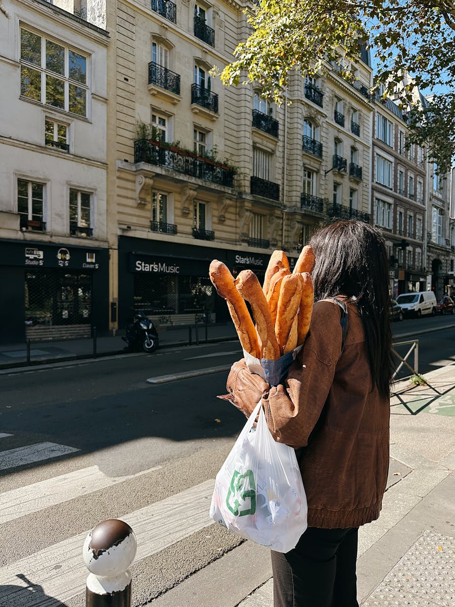 Person walking with baguettes on a Paris street, showcasing city life.