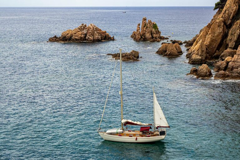 A sailboat glides through the rocky coastline of Blanes, Spain's picturesque seascape.