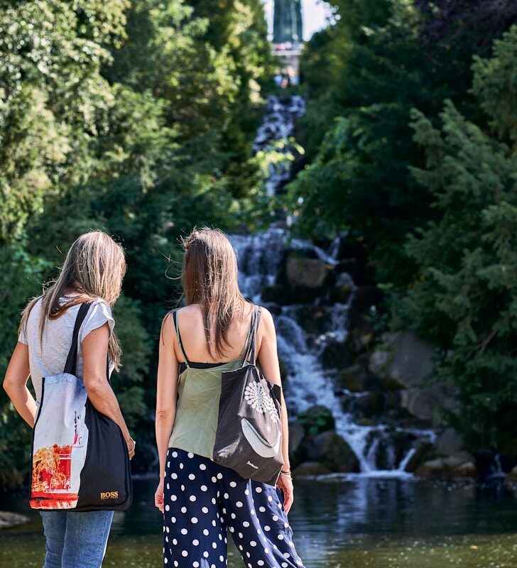 two women standing on the edge of a lake looking at a waterfall